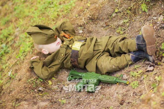 Маленький мальчик в костюме солдата спит на земле, фото